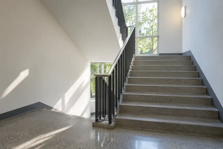 Well lit empty building stairwell with simple handrail.
